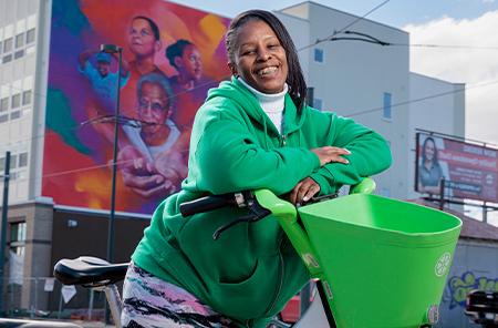 Tasha Clavo sits on a E-Bike in front of a large an colorful mural